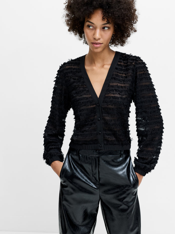 A woman wearing a black semi sheer Blouse with a striped fringe texture, long sleeves, a v-neckline and long sleeves.