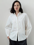 A woman wearing a white cotton Shirt with long balloon sleeves, a pointed collar, a button through fastening, faux pearl drop embellishments and a relaxed fit.