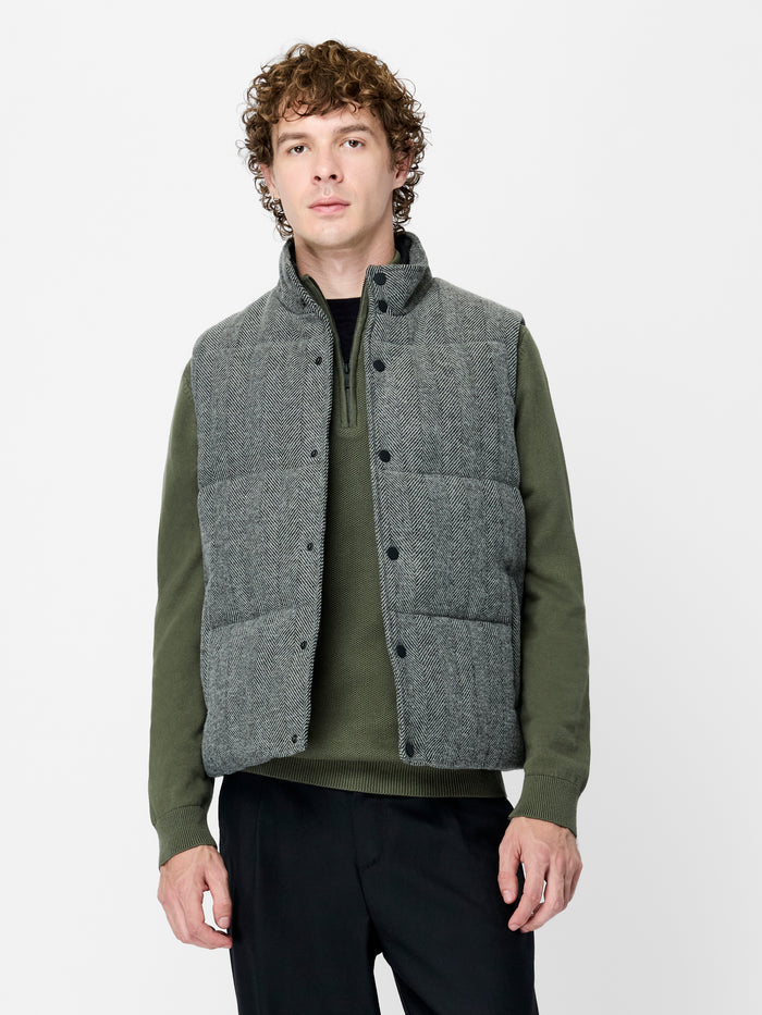 A man wearing a grey quilted waistcoat with side pockets, a button down fastening and a high neckline.