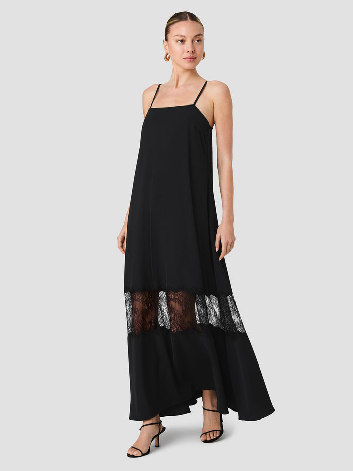 A woman wearing a black maxi length Dress with adjustable straps, a square neckline, a zip zip fastening and a sheer lace panel detailing.