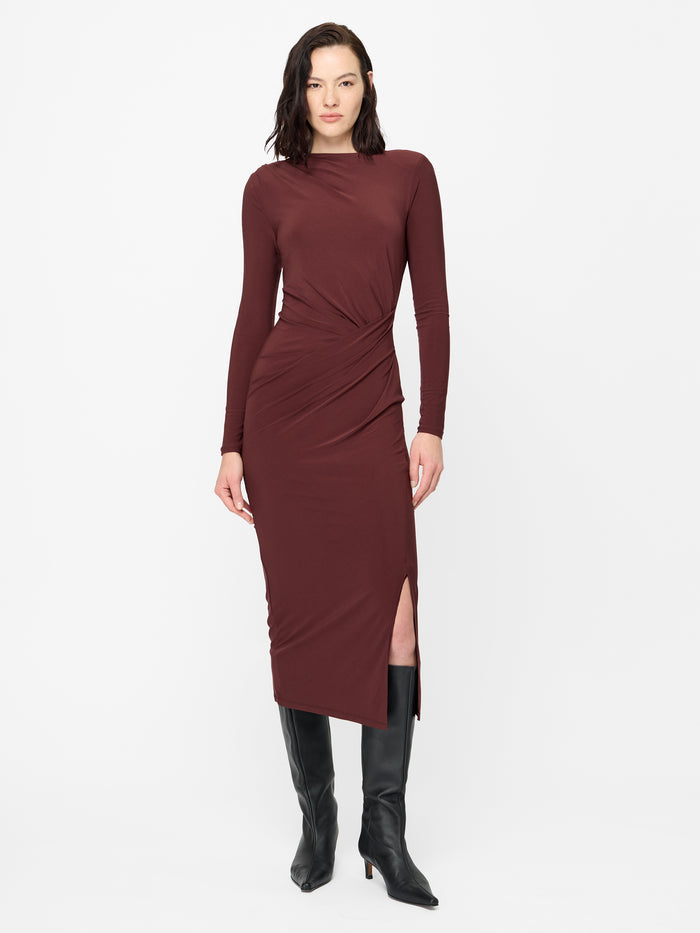 A woman wearing a burgundy midi length Dress with padded shoulders, long sleeves, a crew neckline, draped detailed waist, back keyhole fastening and a side split.